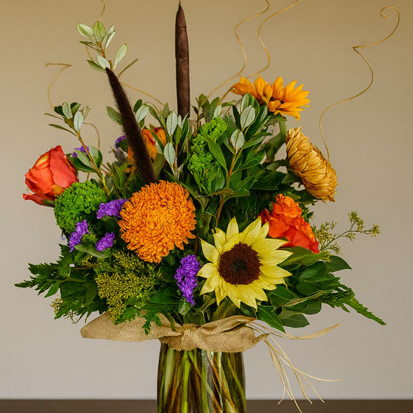 Mixed bouquet in a glass vase with sunflowers, roses, and orange blooms