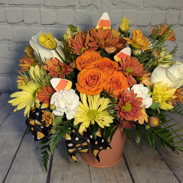 Orange and yellow flower arrangement in a peach vase with a black polka-dot ribbon