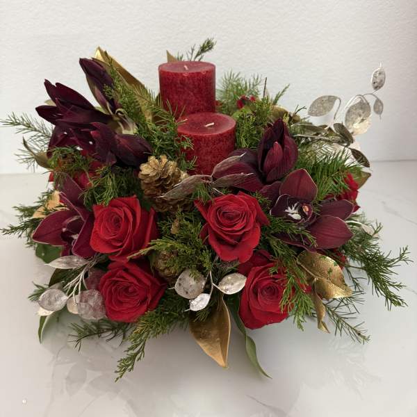 Red roses and burgundy orchids arranged with candles and greenery