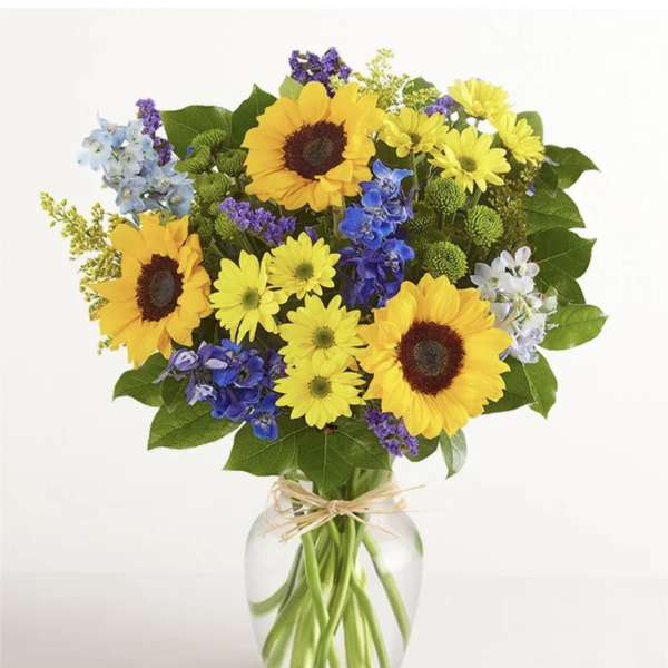 Bouquet of sunflowers, yellow daisies, and blue flowers in a glass vase