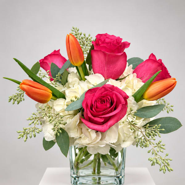 Pink roses and orange tulips in a clear glass vase