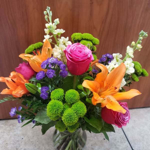 Bouquet of pink roses, orange lilies, and green chrysanthemums in a glass vase