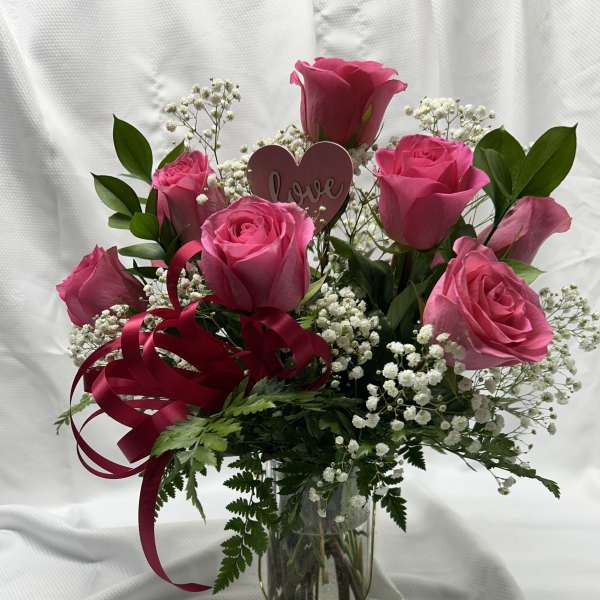 Pink roses in a glass vase with baby's breath and a heart pick