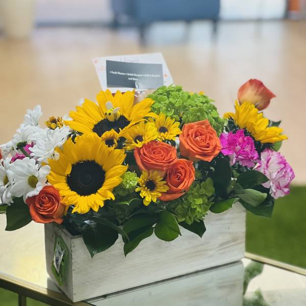 Mixed bouquet in a white wooden box with sunflowers, roses, and daisies