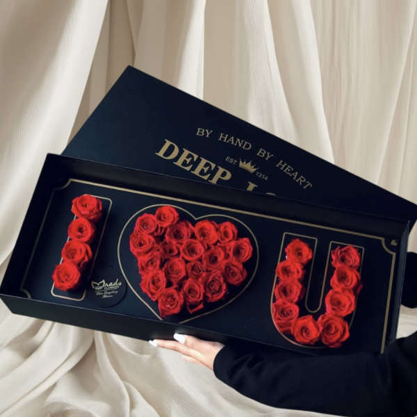 Red roses arranged in a heart and the word LOVE in a black gift box