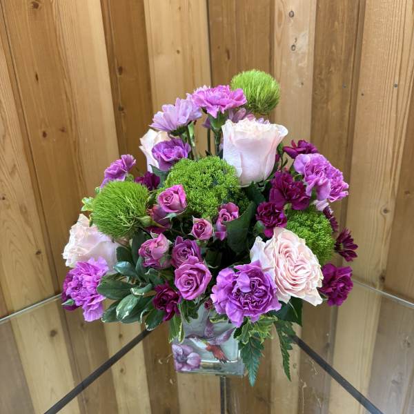 Pink and purple flower arrangement in a square glass vase
