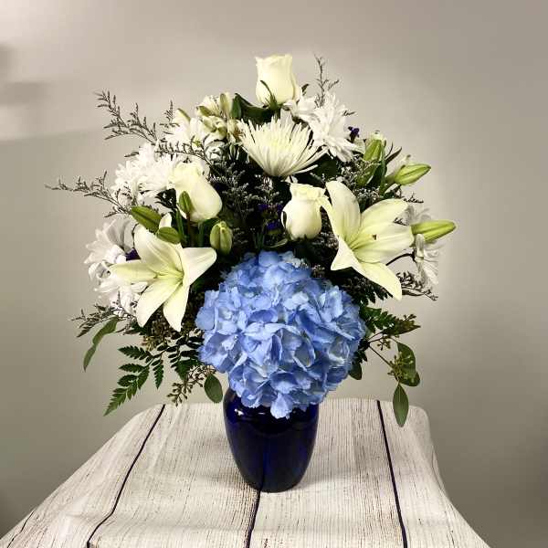 White lilies and daisies with a blue hydrangea in a dark vase