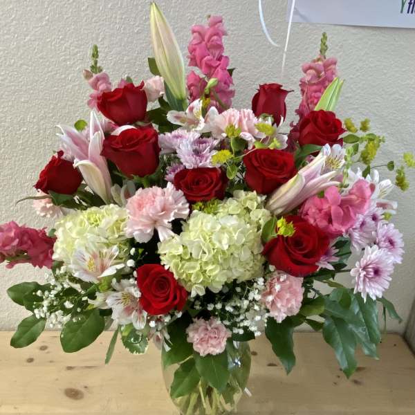 Mixed bouquet of red roses, pink flowers, and white lilies in a glass vase
