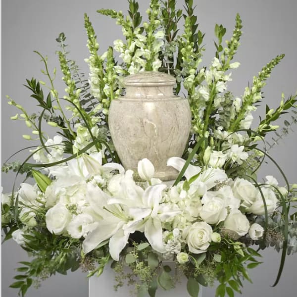 White floral arrangement with lilies and roses around a stone urn