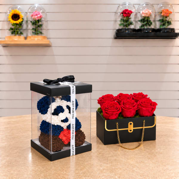 Two boxed rose arrangements, one in a clear gift box and one in a black box with red roses.