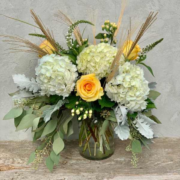 Yellow roses and white hydrangeas in a glass vase with dried grasses