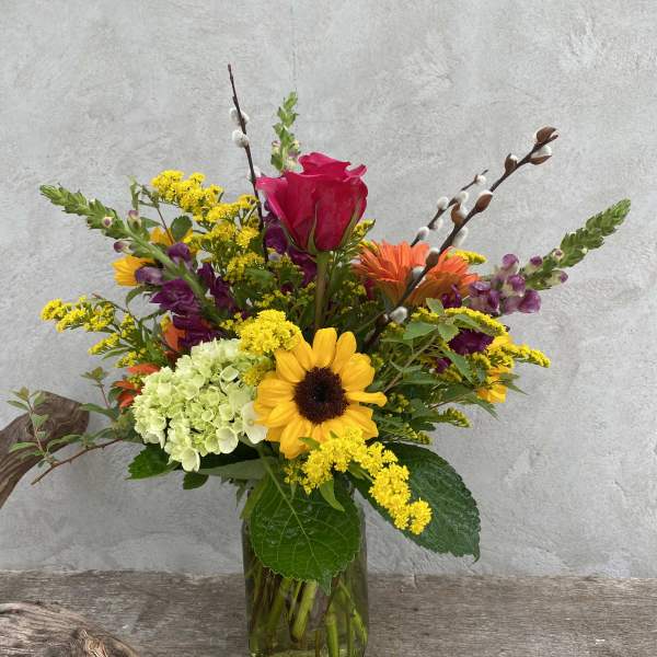Colorful mixed flower arrangement in a glass vase with a sunflower and pink rose