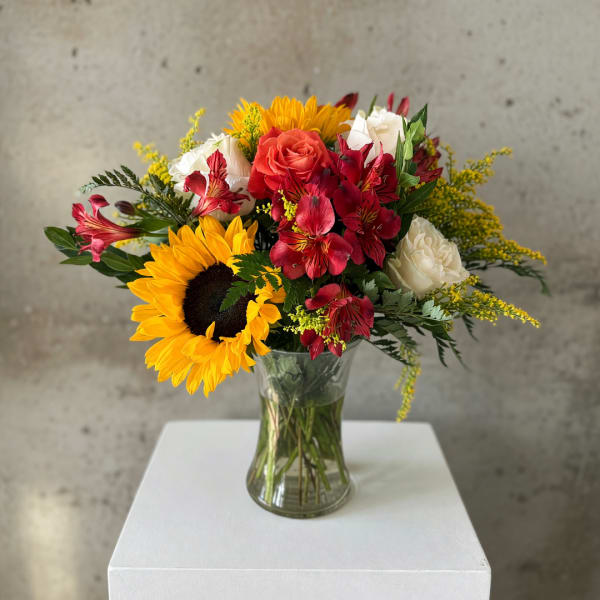 Bouquet of sunflowers, roses, and red alstroemeria in a glass vase