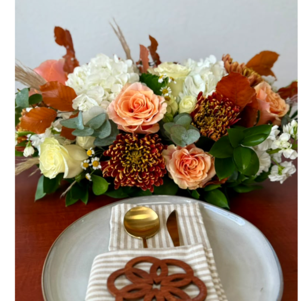 Peach and white floral arrangement with autumn leaves on a table setting