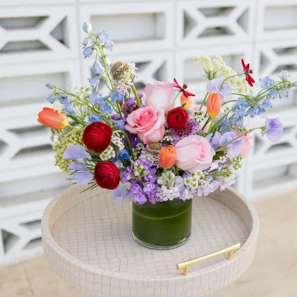 Mixed bouquet of roses, tulips, and blue flowers in a green glass vase