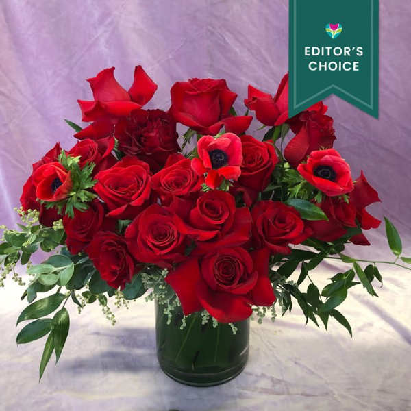 Red rose bouquet in a dark glass vase with green foliage