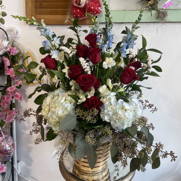 Basket arrangement of red roses, white hydrangeas, and blue flowers