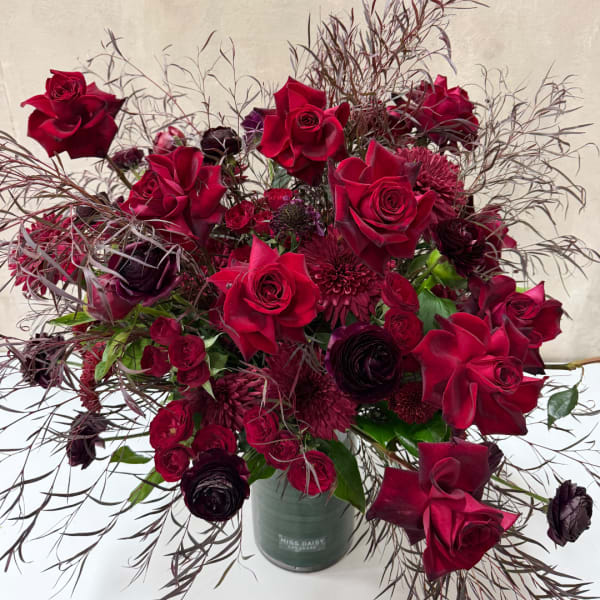 Deep red roses and burgundy blooms in a green vase