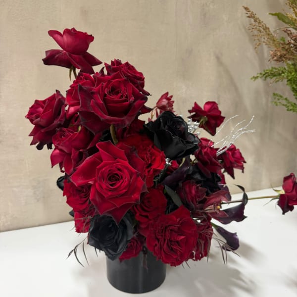 Red and black rose arrangement in a black vase