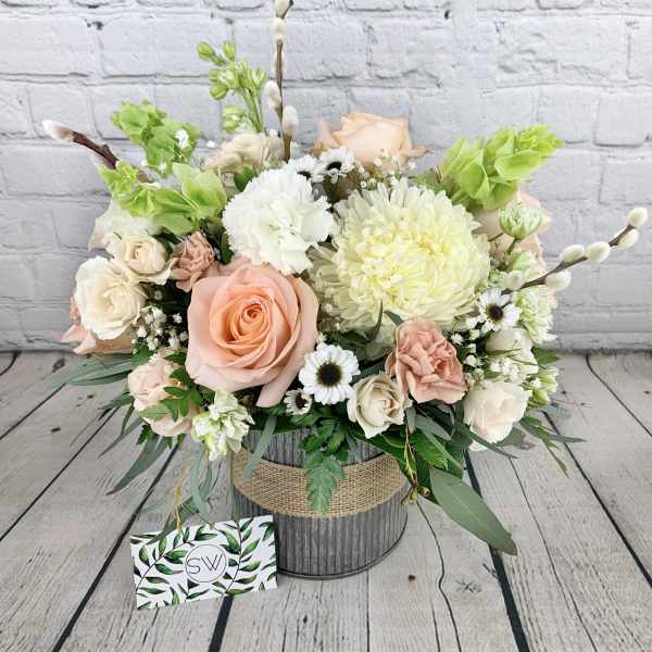 Pastel flower arrangement with roses, chrysanthemums, and daisies in a rustic container