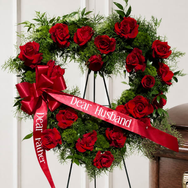 Heart-shaped red rose wreath with a red ribbon on a stand