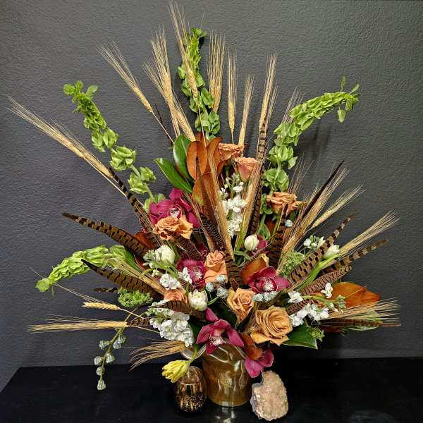 Large tropical bouquet with orchids, roses, and wheat-like stems in a gold vase