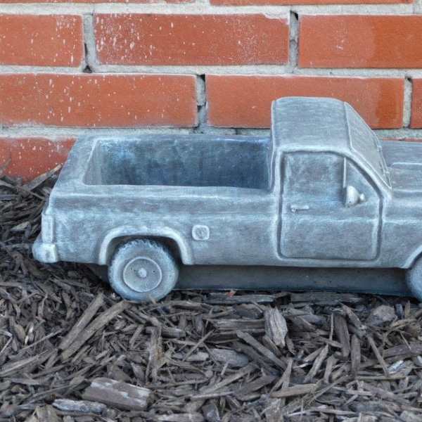 Gray pickup truck-shaped planter on mulch in front of a brick wall
