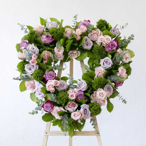 Heart-shaped floral wreath of pink and lavender roses on a wooden stand
