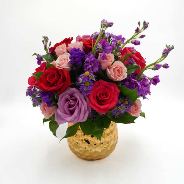 Mixed bouquet of red, pink, and purple roses in a gold vase