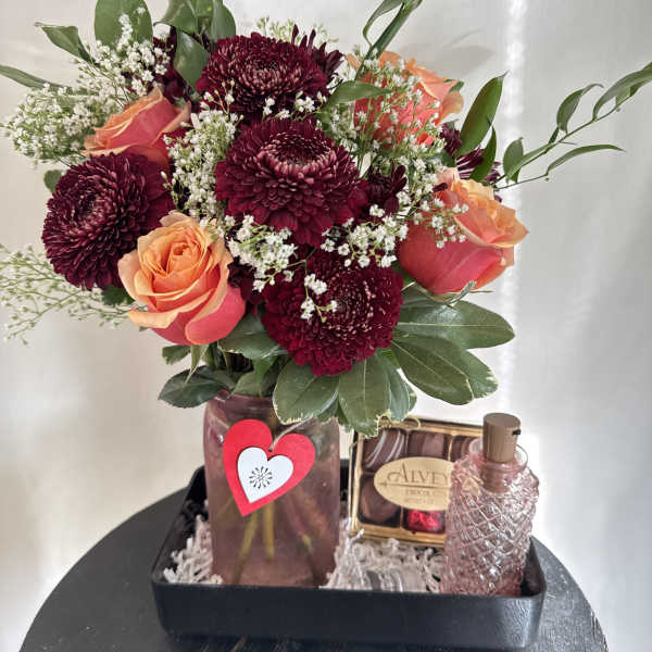 Bouquet of burgundy chrysanthemums and peach roses in a vase with chocolates and perfume