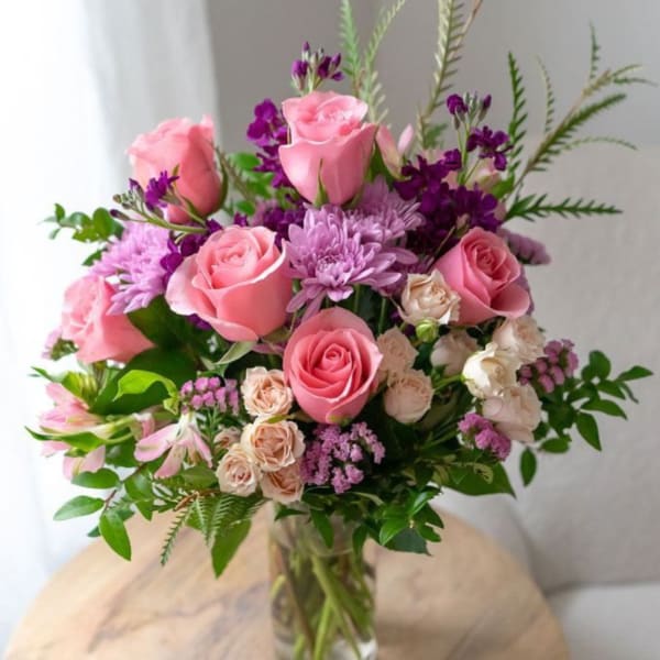 Mixed bouquet of pink roses, lavender mums, and cream spray roses in a clear glass vase