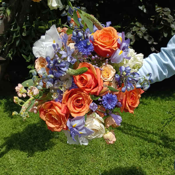Handheld bouquet of orange roses and blue-purple flowers