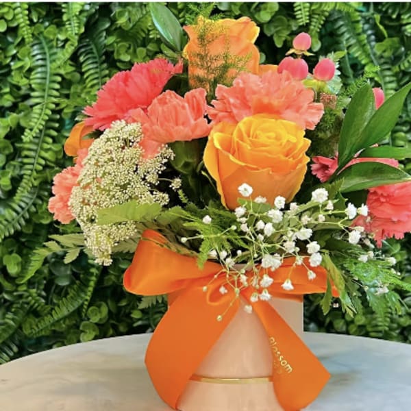 Bouquet of orange and pink flowers in a vase with an orange ribbon