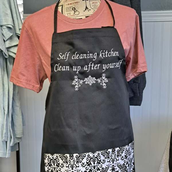 Black apron with white text over a pink shirt