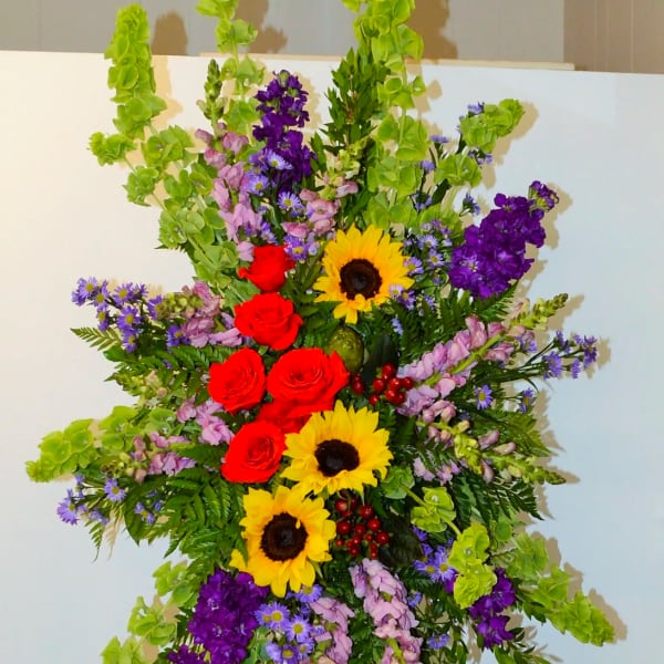 Tall standing floral spray with sunflowers, red roses, and purple blooms