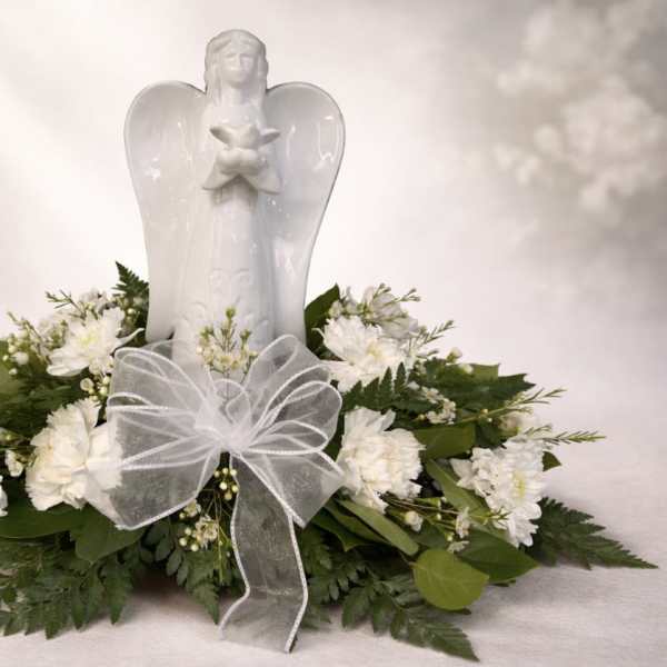 White angel figurine surrounded by white flowers and greenery with a sheer white bow.