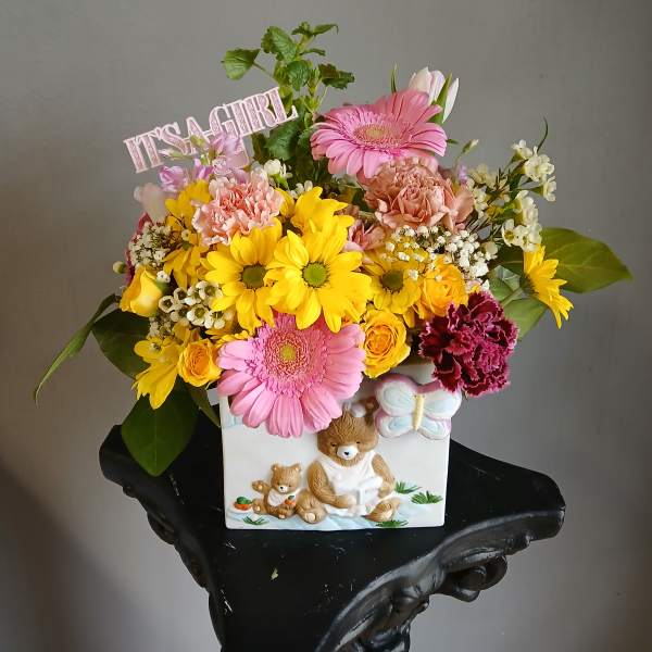 Colorful mixed bouquet in a decorative bear planter with a "IT'S A GIRL" sign