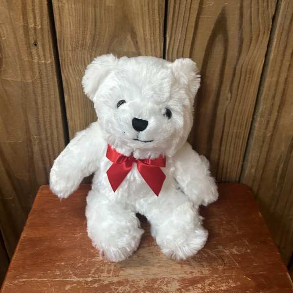 Small white teddy bear with a red bow sitting on a wooden surface.