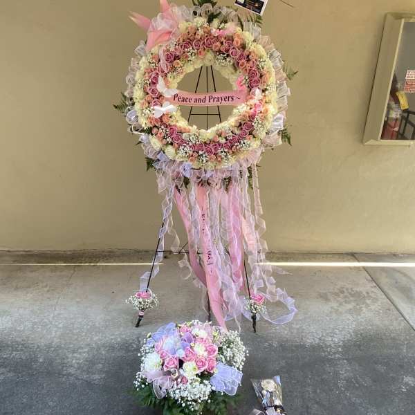 Pink and white floral standing wreath with ribbons and a "Peace and Prayers" sign