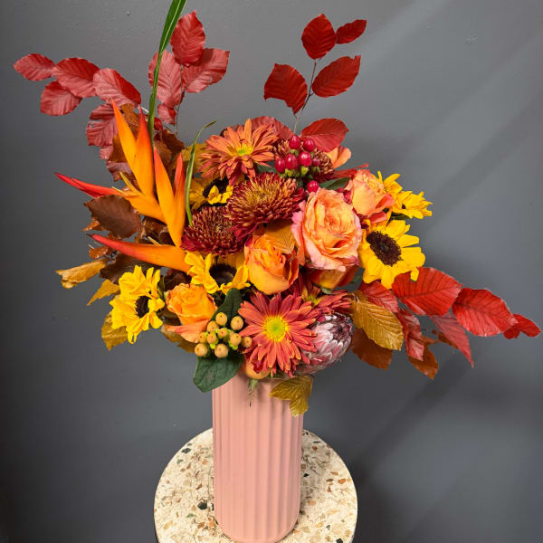 Autumn bouquet with orange roses, sunflowers, and red foliage in a pink vase