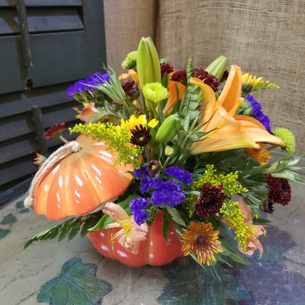Autumn floral arrangement in a pumpkin-shaped container with lilies and chrysanthemums