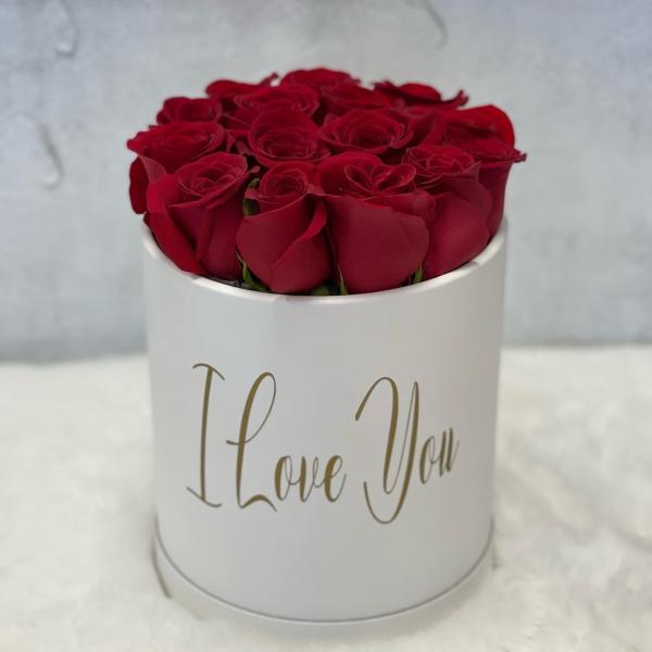 Round white hatbox filled with red roses and gold script reading I Love You.