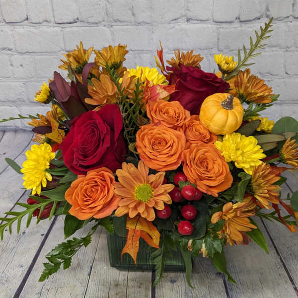Autumn bouquet of orange and red roses with yellow mums in a square vase