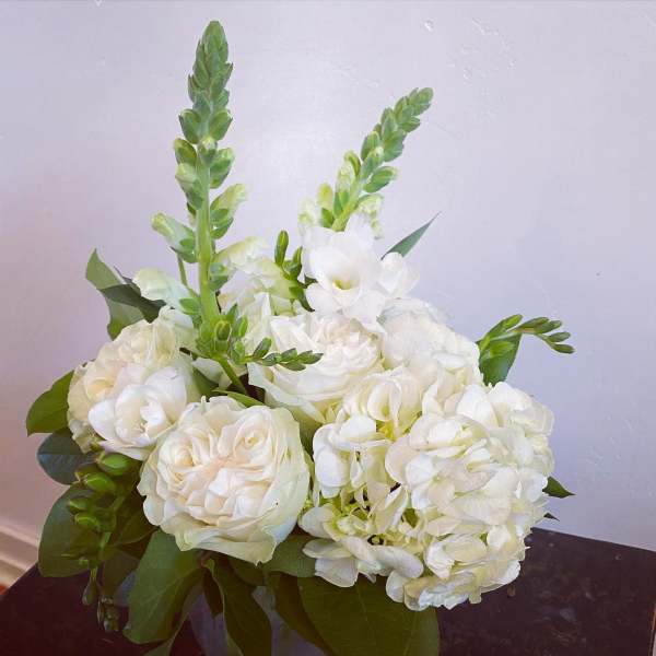 Compact white rose and hydrangea arrangement with snapdragon spikes in a glass vase