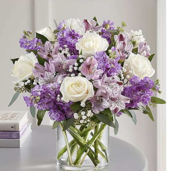 Bouquet of white roses and purple flowers in a clear glass vase
