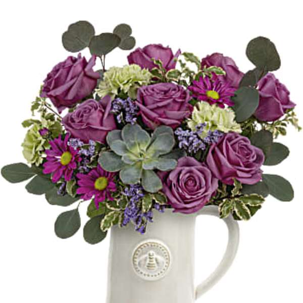 Purple roses and mixed flowers arranged in a white ceramic pitcher