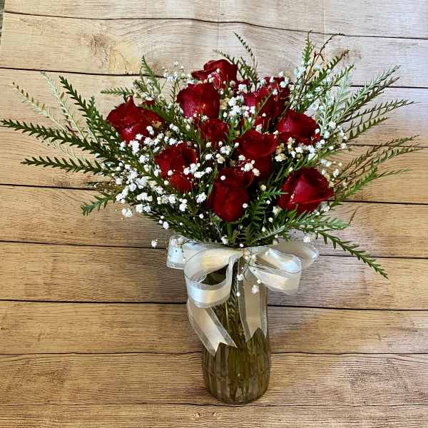 Red roses in a glass vase with white baby's breath and a ribbon bow