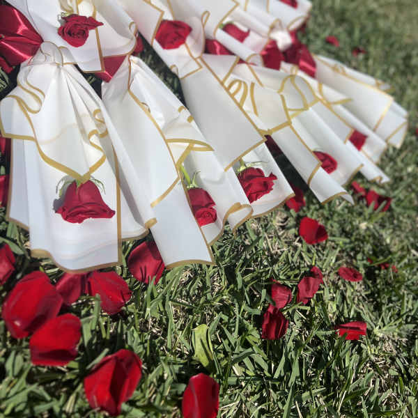 Red roses wrapped in white paper with gold trim and red ribbons on grass