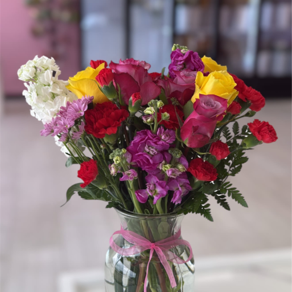 Mixed bouquet of roses and carnations in a glass vase with a pink ribbon