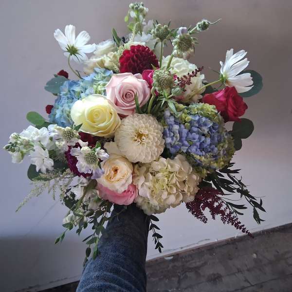 Handheld bouquet of mixed roses, hydrangeas, and white daisies